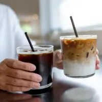 Iced americano vs iced coffee. Woman holding two iced coffee drinks.