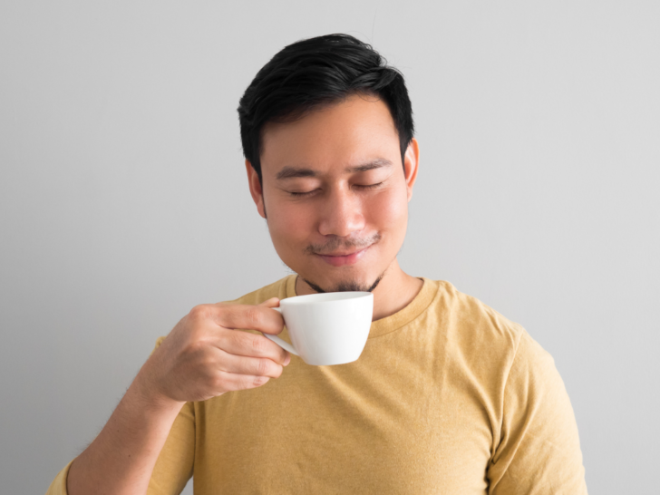 Picture of a man in a yellow shirt holding a coffee cup and enjoying his cup of the best medium roast coffee.
